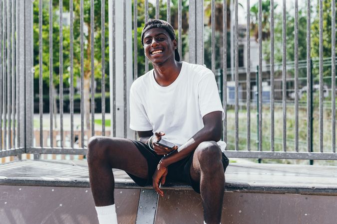Sportive black men browsing smartphone while sitting on fence