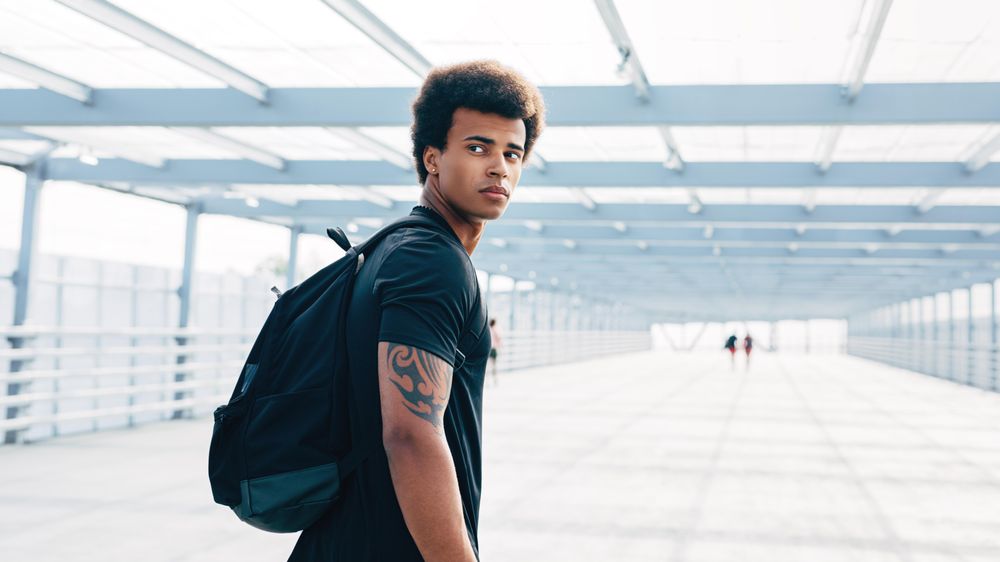 Young Black man walking along bridge with backpack