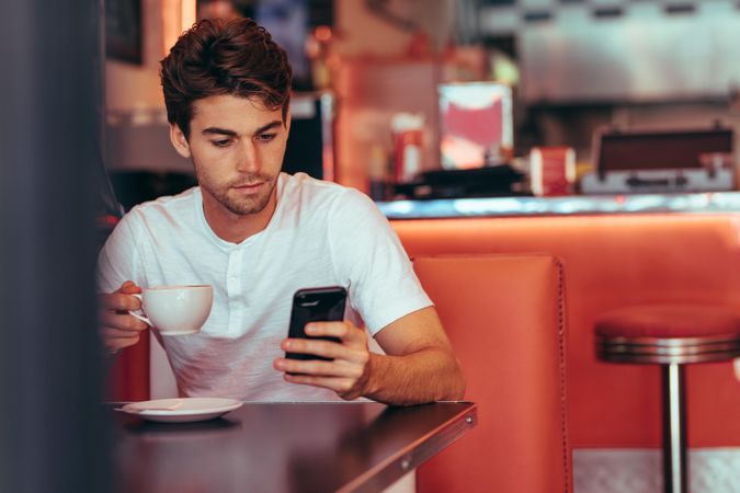 Man checking his cell phone while drinking coffee at a restaurant