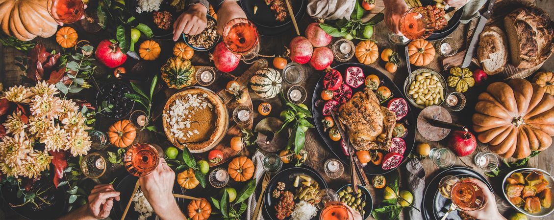 Group of people at festive table setting with roast chicken, squash, and pie, wide composition