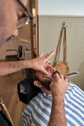 Professional barber trimming beard of client