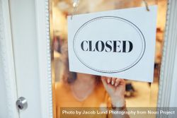 Female owner putting closed sign on her clothing store front door 56aEd0