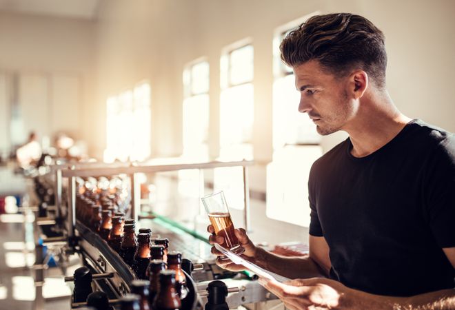 Business owner holding sample of beer in hand and looking at bottled beverages