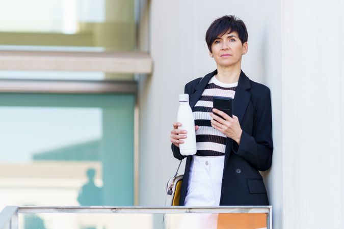 Woman taking break from work standing outside of building with bottle