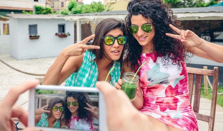 Two female friends with cocktails outside as friend takes photo