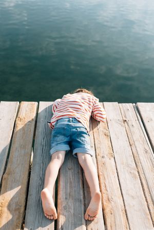 Boy lying on wooden pier in sunlight