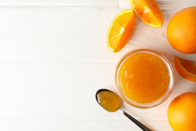 Oranges, spoon and glass jar with jam on wooden background