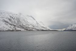 Tranquil lake against snowy hills in cold overcast weather