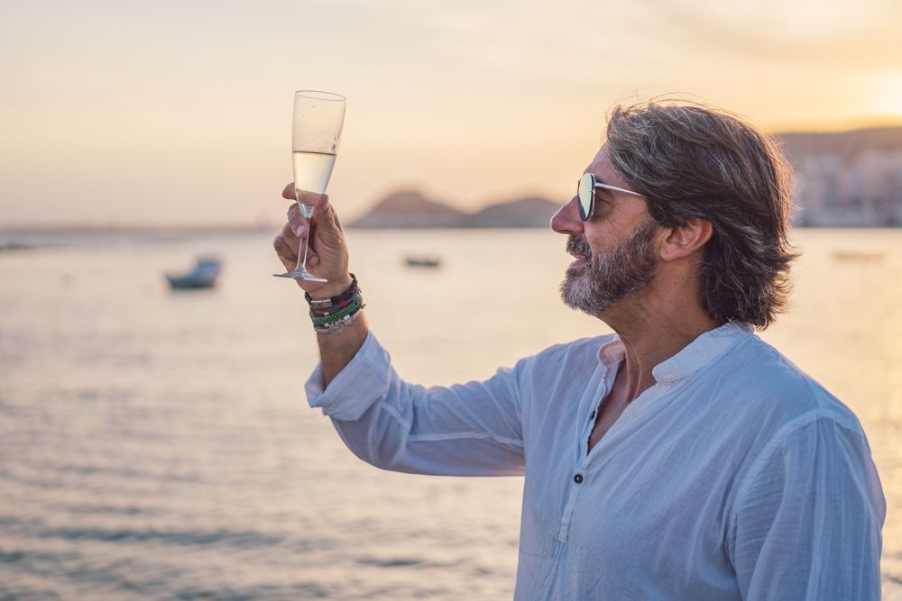 Mature man drinking wine near sea in evening