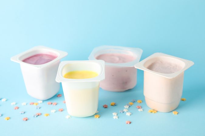 Plastic cups with yogurt and small stars on color background, space for text