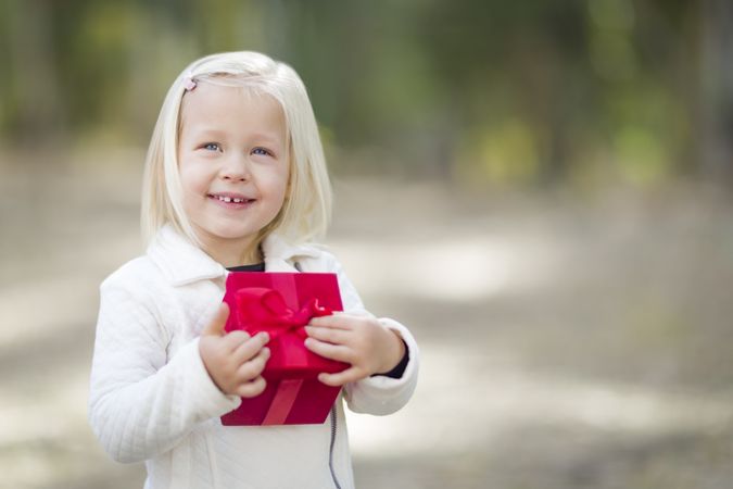 Baby Girl Holding Red Christmas Gift Outdoors