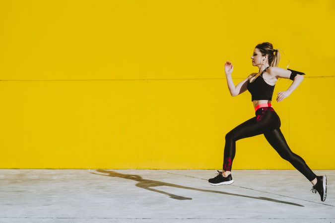Woman with earphones running near wall