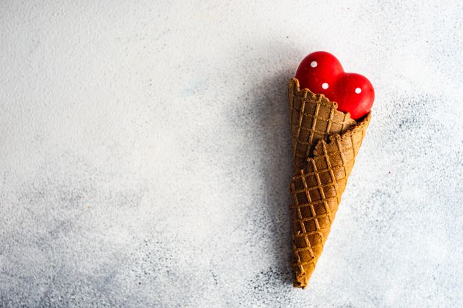 Red heart ornaments in waffle cone on grey background