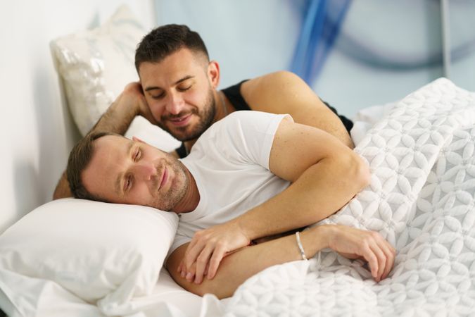Two men holding each other in bed