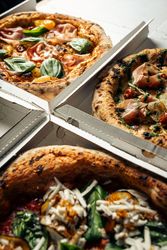Authentic gourmet pizza with basil and toppings in takeout boxes