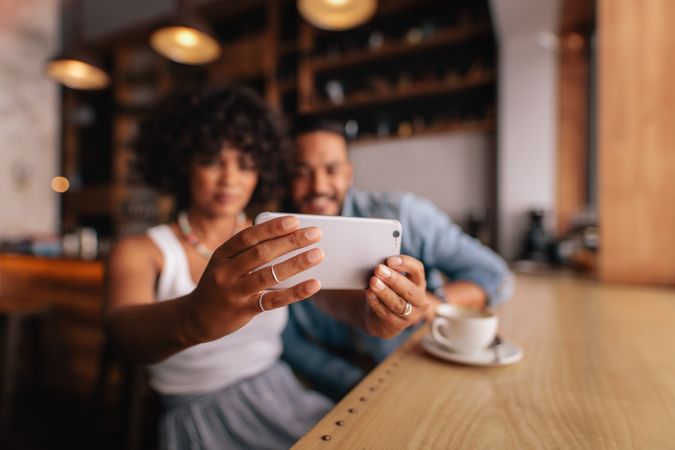 Young woman taking selfie with smart phone while sitting at cafe with her boyfriend