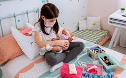Girl with mask playing to take care of her baby doll with mask