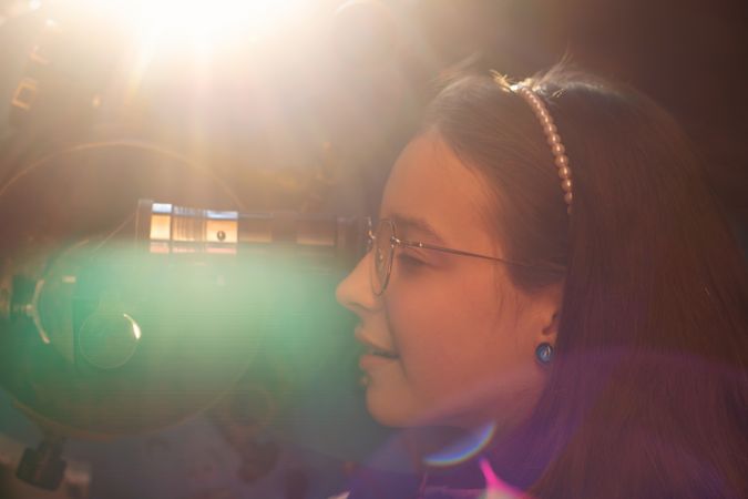 Young girl observes through telescope with sunlight flare.
