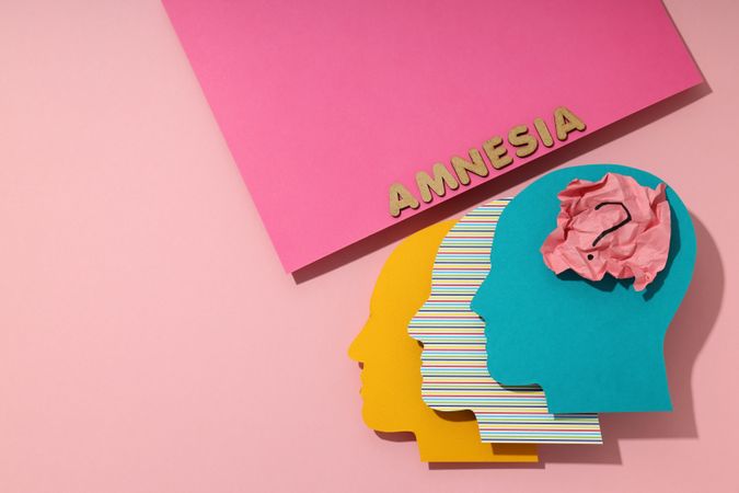 Paper cut outs of colorful head on pink background with the word “Amnesia” with copy space