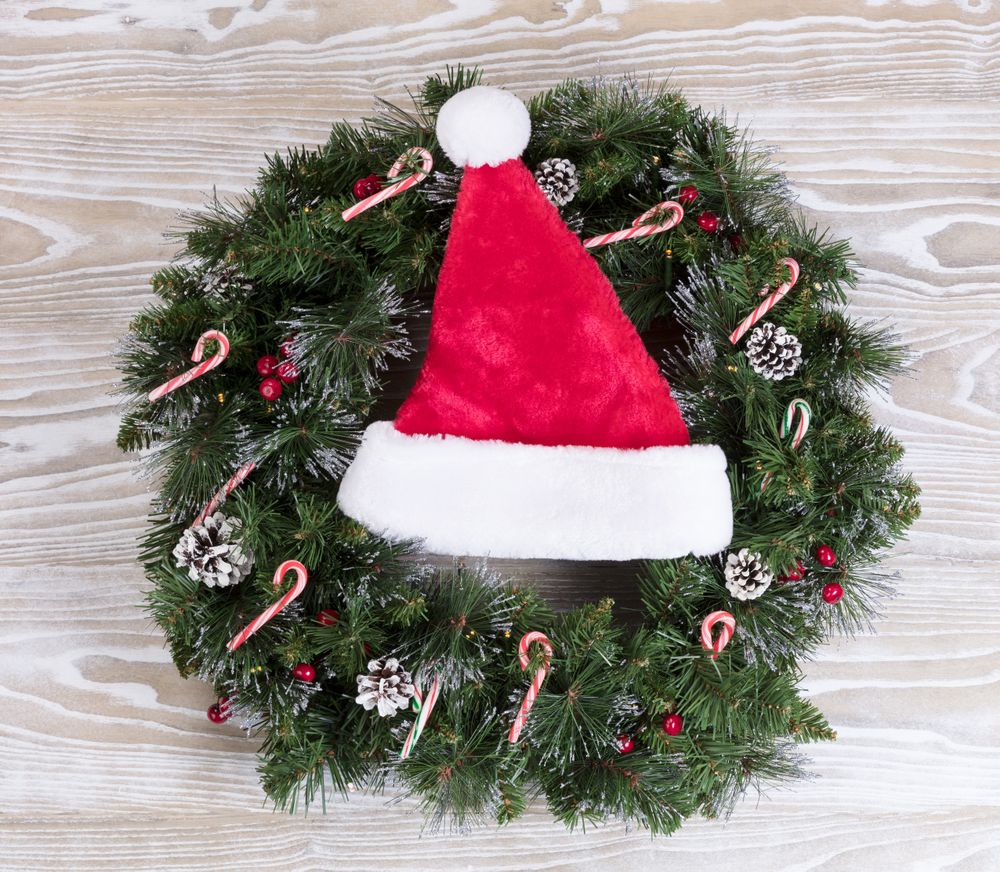 Christmas wreath and Santa cap with lights and candy canes on wooden boards