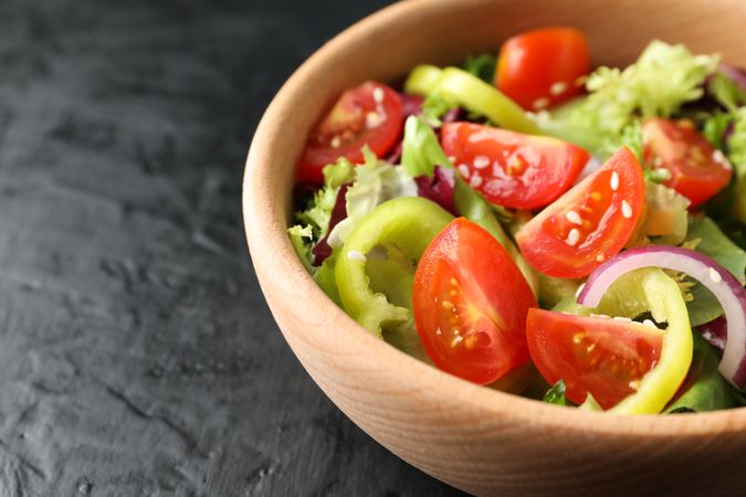 Wooden plate with salad on dark background, close up