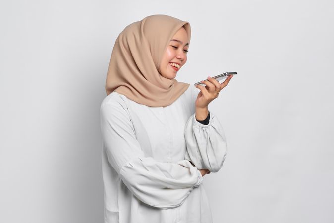 Asian Muslim woman smiling while having a conversation on her cell phone using the speaker phone