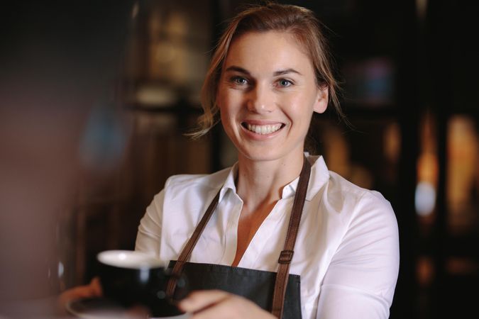 Smiling woman serving coffee inside a coffee shop