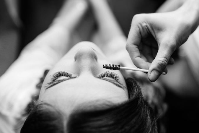 Grayscale photo of person applying a mascara on woman's eyelashes