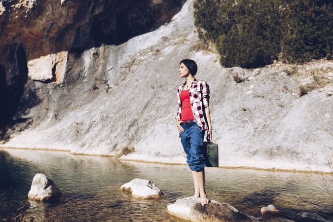 woman standing on rock with case near clear water in lake