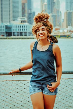 Happy Black woman at waterfront in Brooklyn with Hudson River in background, vertical