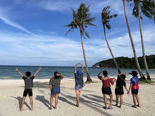 Back view of young people standing on sandy beach near palm trees