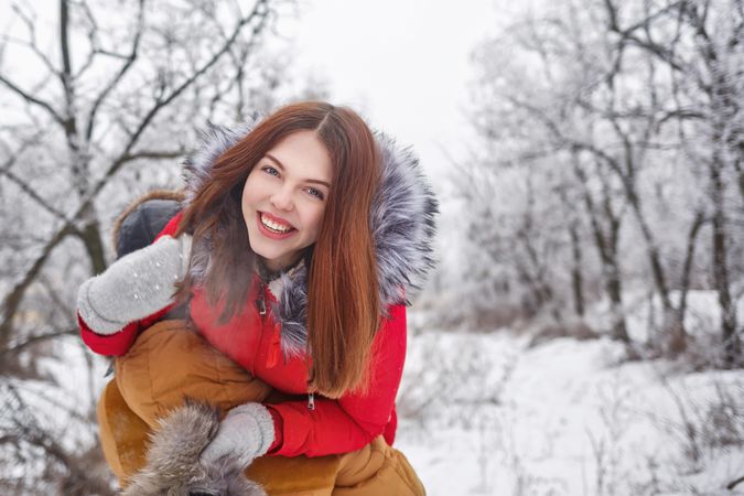 Teenage girl happy and hanging off other person’s shoulder in snowy forest