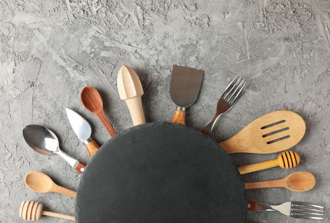 Composition with different kitchen cutlery and round cutting board on gray background