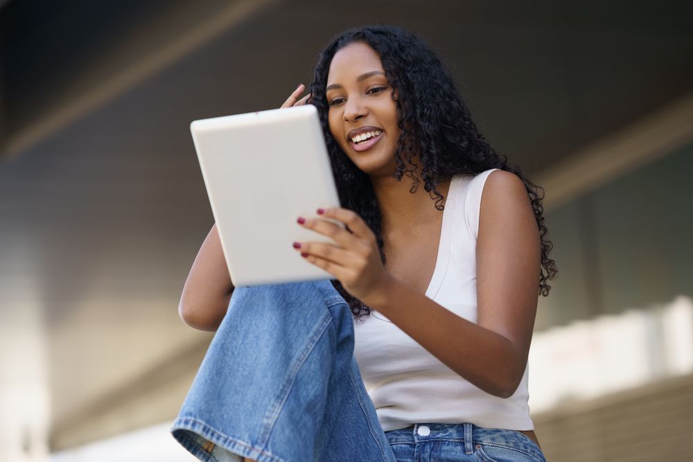A young woman is engaging with her tablet in a relaxed and casual outdoor setting