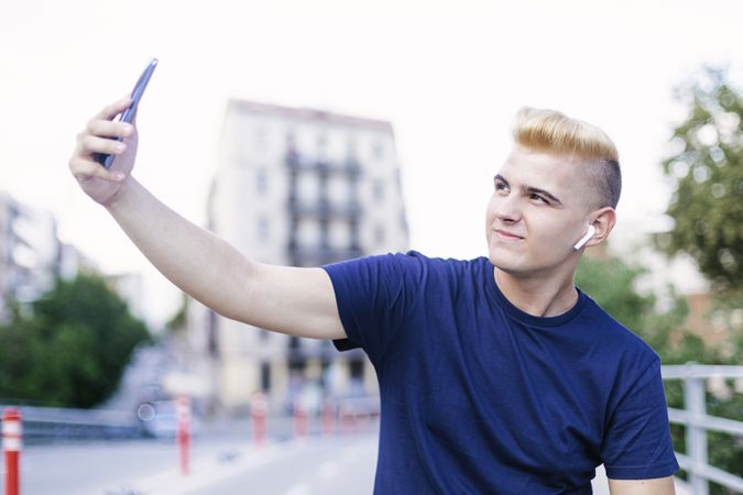 Young blond man sitting outdoors and taking a selfie
