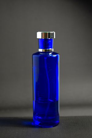 Blue perfume bottle in grey studio with copy space