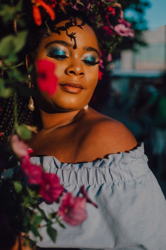 Joyful trendy Black woman standing beside blossomed tree