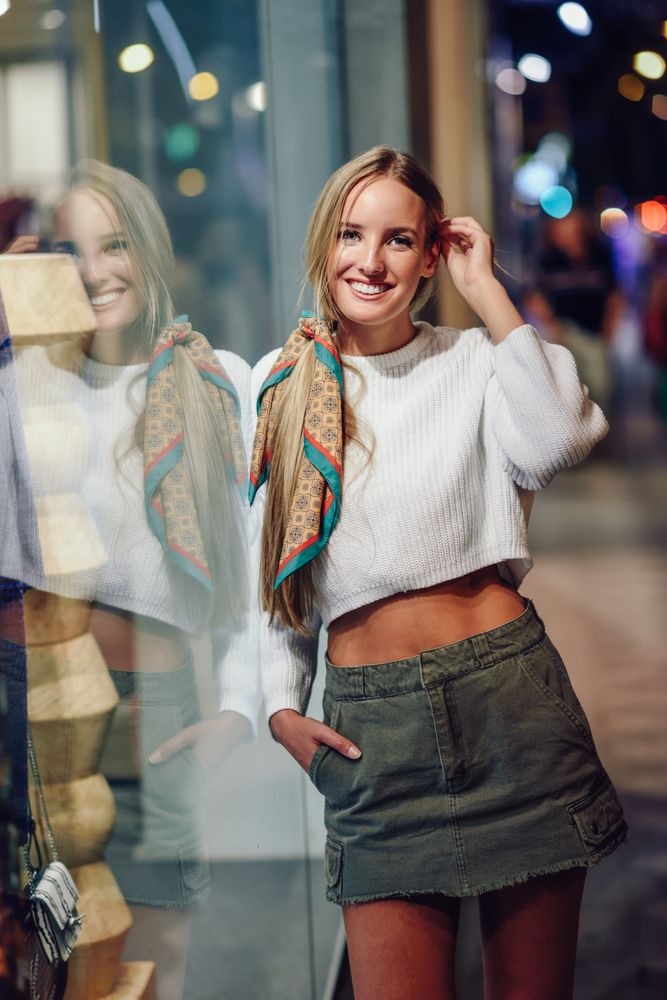 Blonde woman fixing hair next to shop window at night, vertical