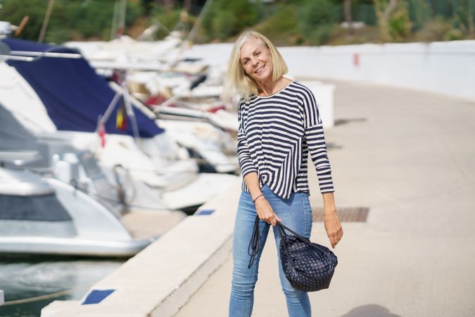 Carefree older woman in jeans and striped shirt standing outside on sunny day