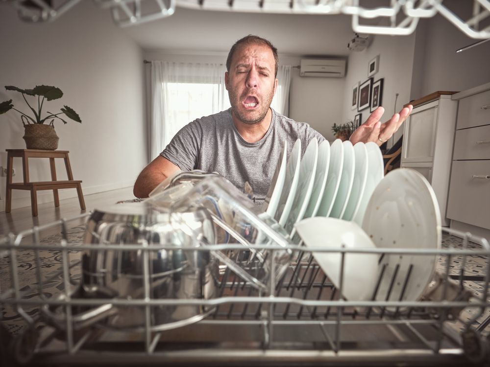 Unhappy man near modern dishwasher