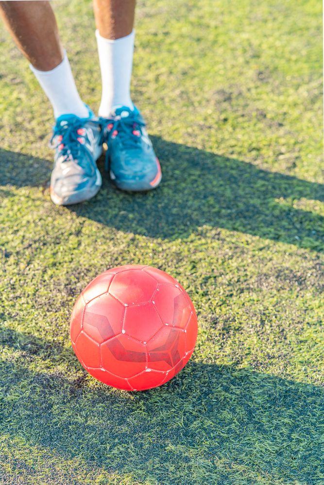 Football ball on lawn near anonymous athlete