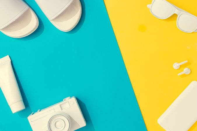 Summer objects of flip flops, sunglasses, camera, smart phone, EarPods on blue and yellow background