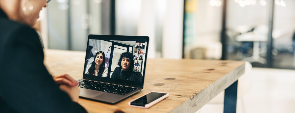 Young businesswoman attending a virtual meeting in a modern office with two coworkers on laptop