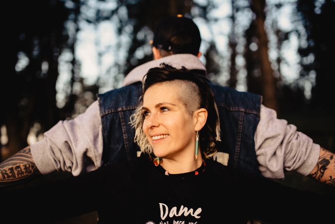 Young guy and happy woman standing back to back in forest