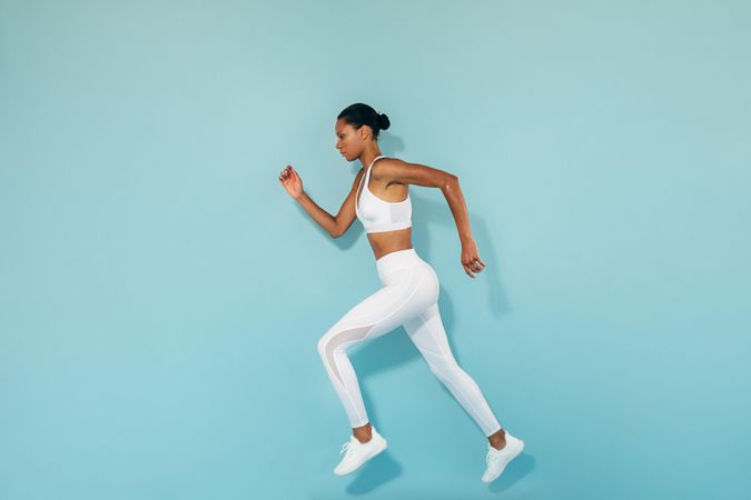 Full body shot of athletic woman sprinting against blue background, side view