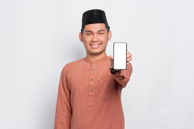 Muslim man in kufi hat smiling and presenting blank screen on mobile phone