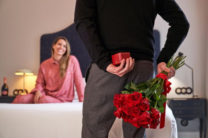 Person with gift and flowers against waiting girlfriend in hotel