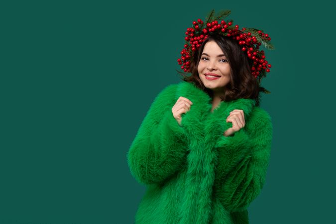 Smiling woman in green coat and red berry wreath posing.