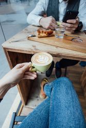Hand holding cappuccino with latte art over cafe table