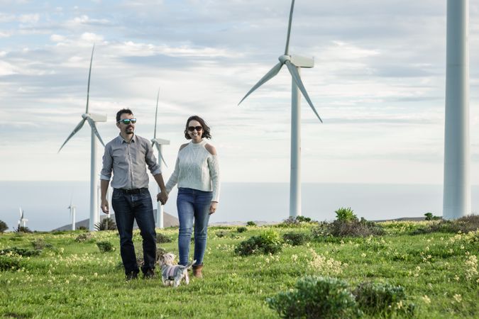 Man and woman holding hands and standing near wind turbines